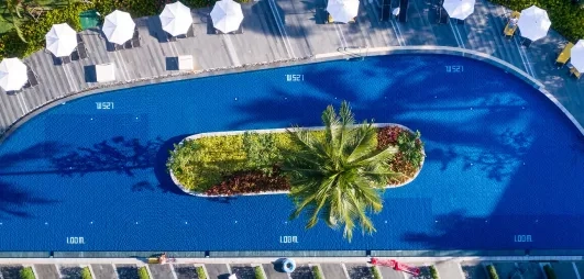 Une large piscine entourée de palmiers et de jardins tropicaux au coucher du soleil.