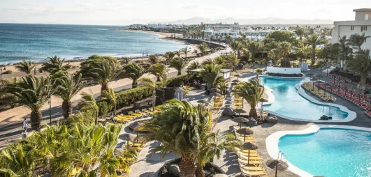 Une vue en hauteur montrant une longue piscine qui s'étend vers une plage, bordée par l'océan bleu.