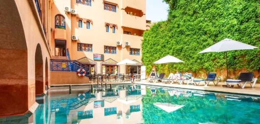 Une vue sur la piscine de l'hôtel, encadrée par un bâtiment moderne aux murs ocre et un grand mur végétal.