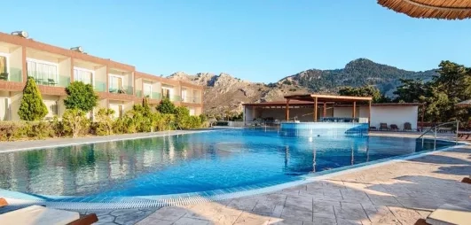 piscine transats, bâtiments hôtel un étage avec balcons, montagnes en arrière-plan, ciel bleu