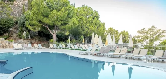 Une piscine aux eaux turquoise bordée de transats et de végétations verdoyants. 