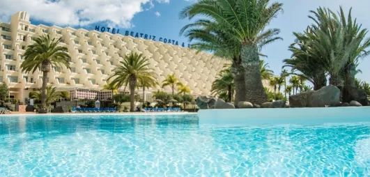 Vue sur la façade du bâtiment et la végétation tropicale qui entoure le bassin.