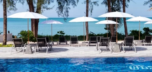 Vue d'une piscine bordée de palmiers avec des parasols blancs, des transats.