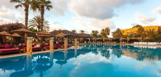 Grande piscine entourée de palmiers, transats confortables et ambiance ensoleillée