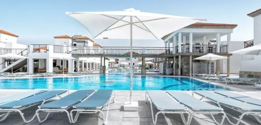 Une vaste piscine ensoleillée bordée de transats confortables et d'un grand parasol blanc..
