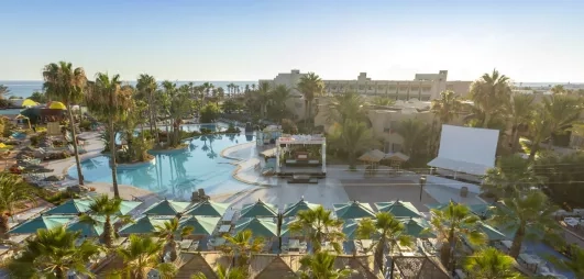 Vue panoramique des infrastructures, piscines et jardins luxuriants de l'hôtel Welcome Meridiana à Djerba en bord de mer.