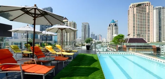 Un rooftop moderne avec piscine, pelouse et transats offrant une vue panoramique sur la ville.