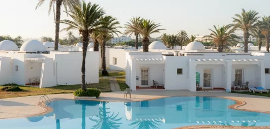 Bungalows blancs typiques et piscine azur entourés de jardins au One Resort Aqua Park à Monastir.
