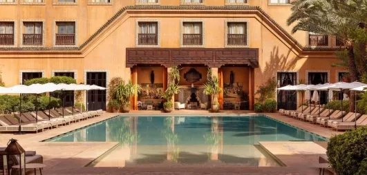 Vue Générale sur la piscine extérieure avec des transats au bord de la piscine et un salon marocain à toit couvert  