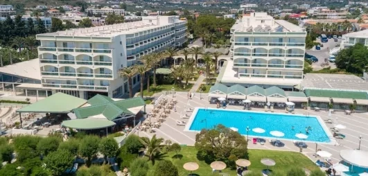 grande piscine, deux bâtiments de quatre étages avec balcons, transats et parasols palmiers, végétation luxuriante