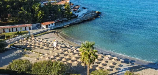 Une vue plongeante sur une plage avec de nombreux parasols alignés au bord d'une eau turquoise.