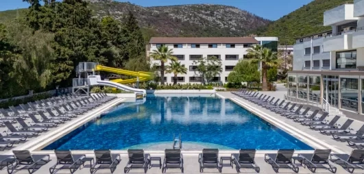 Une vue d'une grande piscine entourée de nombreux transats, avec les bâtiments de l'hôtel.