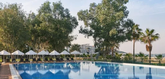 Une piscine bordée de parasols blancs et de grands arbres verdoyants.
