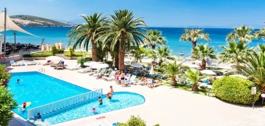 Une vue plongeante sur la piscine, bordée de palmiers avec la mer en arrière-plan.
