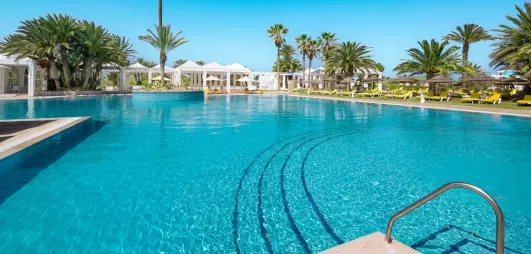 Grande piscine extérieure entourée de palmiers et de transats sous le soleil au Djerba Golf.