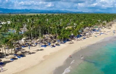 Vue plage de sable blanc, eau turquoise, palmiers, transats bleus, piscine