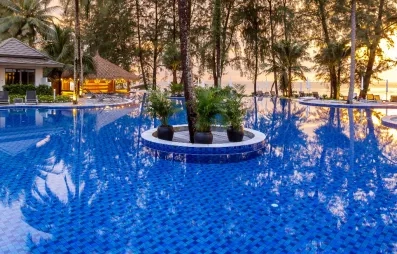 Une large piscine entourée de palmiers et de jardins tropicaux au coucher du soleil.