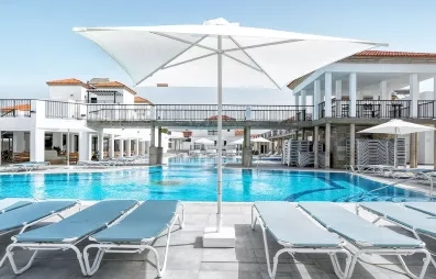 Une vaste piscine ensoleillée bordée de transats confortables et d'un grand parasol blanc..