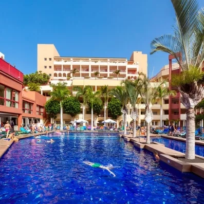 Vue sur la piscine principale bordée de palmiers et l'architecture étagée de l'hôtel.