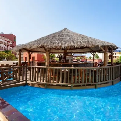 Un bar de piscine au toit de chaume de style paillote est installé juste au bord de l'eau turquoise.