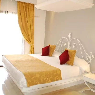 Chambre lumineuse avec lit double, tête de lit en fer forgé blanc et rideaux jaunes au Djerba Aqua Resort.