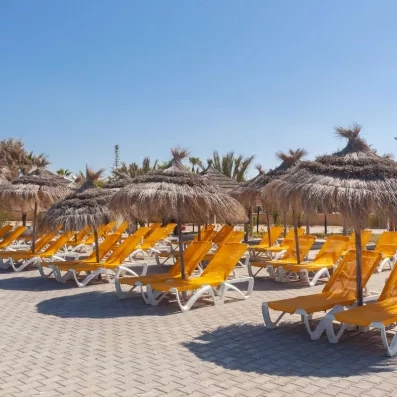 Transats jaunes et parasols en paille alignés sur la terrasse ensoleillée du Djerba Aqua Resort en Tunisie.