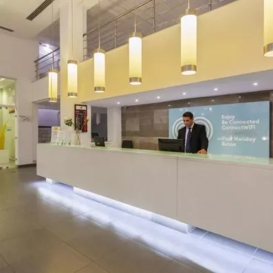 Réceptionniste accueillant les voyageurs au comptoir moderne et lumineux du hall d'entrée du Djerba Aqua Resort.