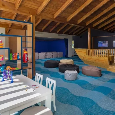 mini-club pour les petits, poufs disposés au centre, bateau en bois taille réelle sur la droite, étagères et table et chaises avec jeux posés dessus