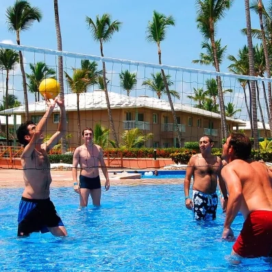 groupe d'hommes jouant au volley ball dans la piscine, palmiers, ciel bleu
