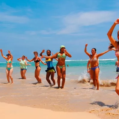 groupe de femmes dansant sur la plage de sable, océan en arrière plan, eau turquoise, ciel bleu