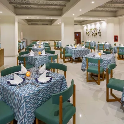 salle de restaurant tables carrées nappe bleue et chaises en velours vert, murs blancs avec quelques décorations latines