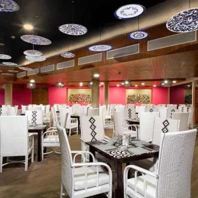 salle de restaurant tables carrées bois foncé et longues chaises blanches avec accoudoirs, murs rouges, plafond en bois