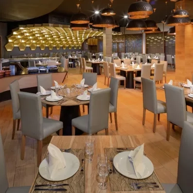 salle de restaurant chaises grises tables rondes en bois, parquet bois au sol et gros luminaires gris circulaires au plafond