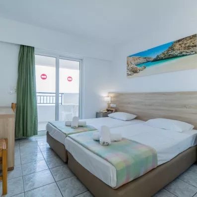 Chambre avec deux lits collés, une tête de lit en bois, un tableau d'une plage et une porte fenêtre de la terrasse