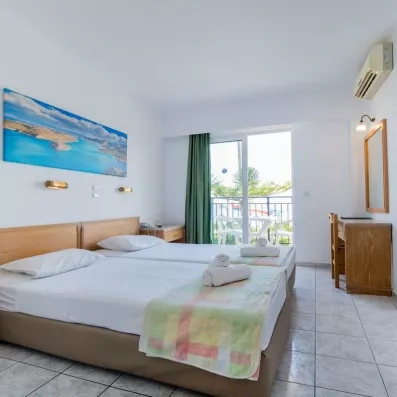 Chambre avec deux lits collés, une tête de lit en bois, un tableau d'une plage et une porte fenêtre de la terrasse