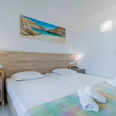 Chambre avec deux lits collés, une tête de lit en bois, un tableau d'une plage et une porte fenêtre de la terrasse