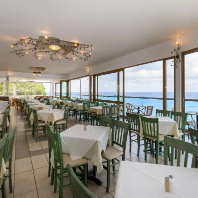salle de restaurant donnant sur la plage avec des chaises vertes en bois et des tables dressées