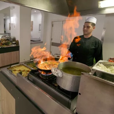 cuisinier portant l'uniforme entrain de flamber un plat à côté du buffet