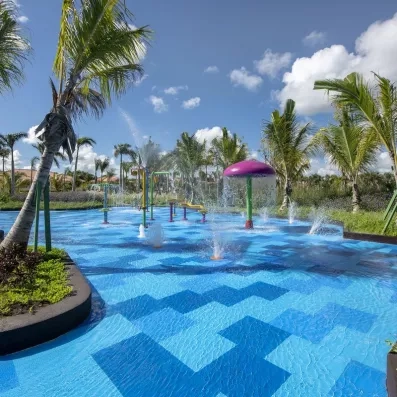 piscine avec jeux d'eau multicolores pour les petits enfants, palmiers tout autour, ciel bleu et nuages