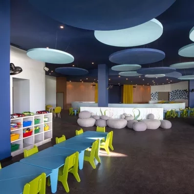 salle de jeu pour enfants, gros poufs en forme de pierres avec un décor sous-marin, petites tables bleues et petites chaises vertes, rangements pour des petites voitures