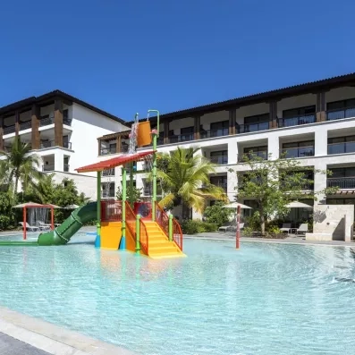 pataugeoire avec petit escalier et toboggan vert pour enfants, bâtiment de l'hôtel avec des balcons, transats, parasols