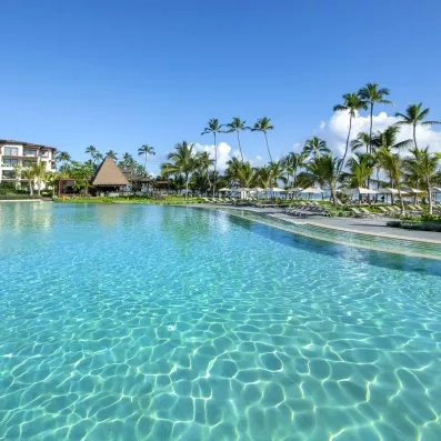 piscines avec palmiers et mer derrière, plage de sable, transats et parasols