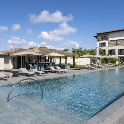 piscine eau translucide, pool bar, transats et parasols beige, bâtiment de l'hôtel avec des balcons