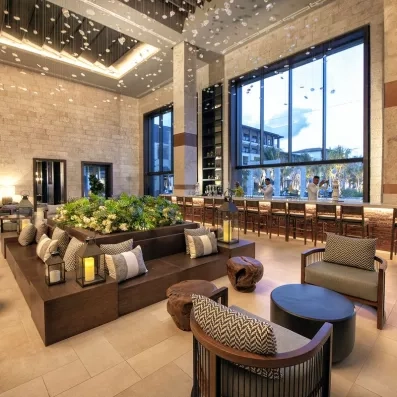 hall d'accueil, canapés et fauteuils, architecture coloniale, grande baies vitrées derrière l'accueil, plantes vertes au centre de la pièce