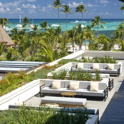 vue terrasse et mer, canapés gris avec des coussins blancs cassés, des petites tables en bois, plantes, végétation luxuriante, pieds dans l'eau