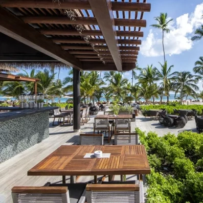 bar terrasse, tables carrées en bois, chaises et fauteuils, palmiers, ciel bleu, nuages, végétation