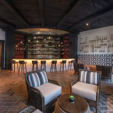 bar salon, fauteuils beige, décoration bois foncé, chaises hautes de bar, luminaires ronds bas et sombres, bouteilles