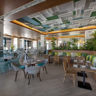 salle de restaurant, chaises confortables, tables en bois carrées, luminaires bas, piliers carrés blanc et verts, décoration volets blancs verts et bleus au plafond