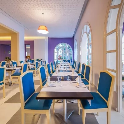 Restaurant moderne aux chaises bleues et murs violets avec vue jardin au Marhaba Beach à Monastir.