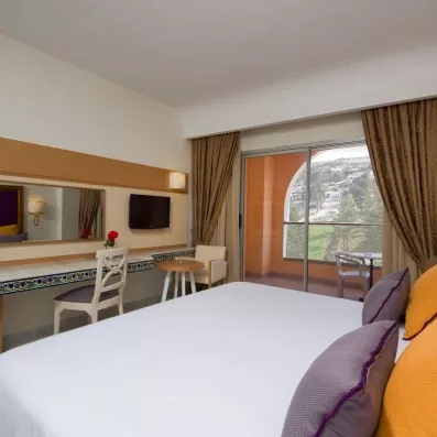 Intérieur de chambre tout confort avec coin bureau, télévision et vue sur les jardins du Marhaba Palace.